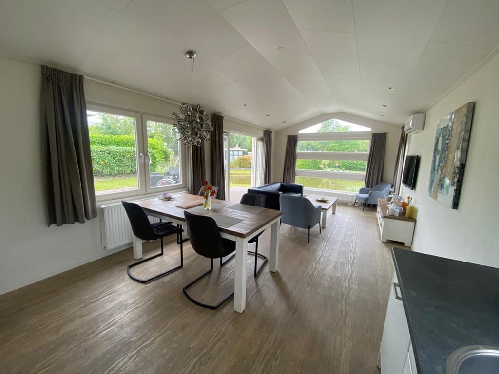 Ruime woonkamer met eetgedeelte, banken en grote ramen met uitzicht op de tuin en omgeving.