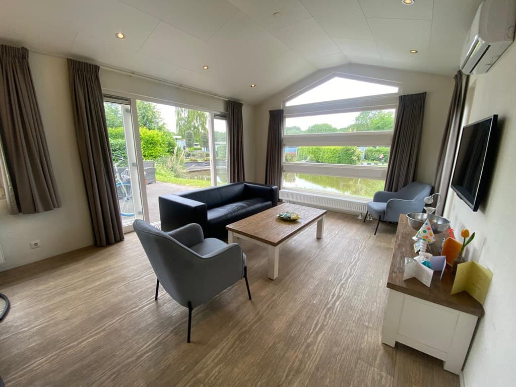 Woonkamer met bank, fauteuils, tafel en grote ramen met uitzicht op de tuin en het water