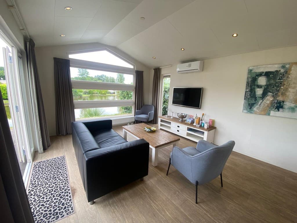 Woonkamer met moderne meubels, tv, grote ramen en uitzicht op het water en de tuin