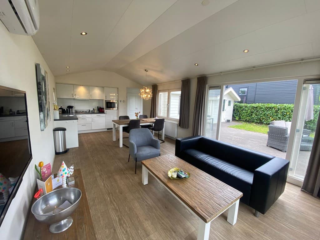 Moderne woonkamer met open keuken, grote ramen en toegang tot een terras met tuinmeubilair.