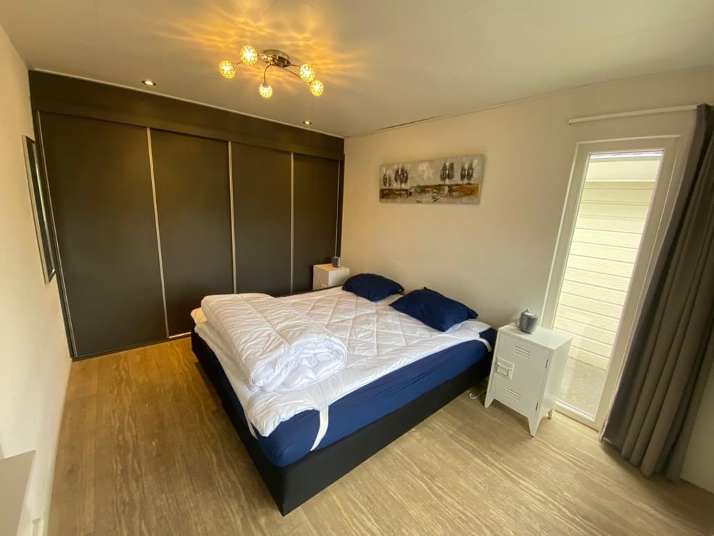 Slaapkamer met groot bed, donkere kast, houten vloer en toegang tot een deur naar buiten.