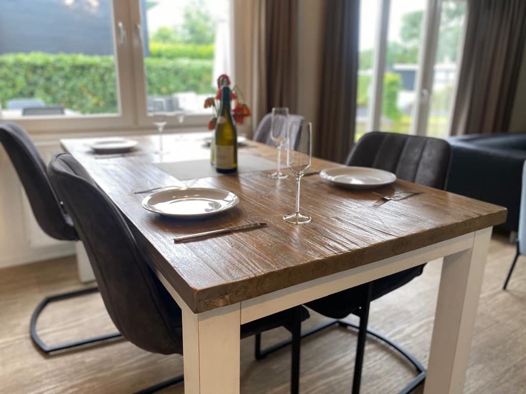 Eettafel met houten blad, glazen, borden en een fles wijn, omringd door moderne stoelen met een lichte achtergrond.