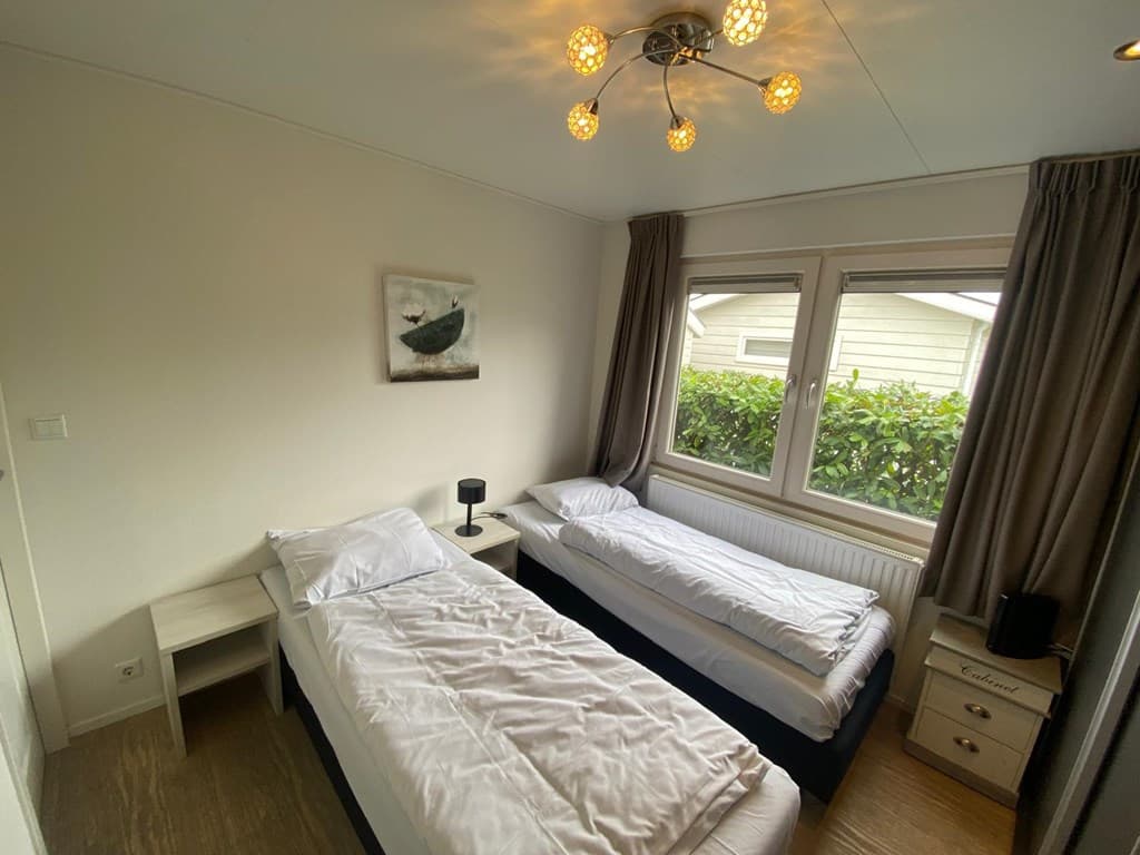 Slaapkamer met twee aparte bedden, een nachtkastje en raam met uitzicht op groene heg.