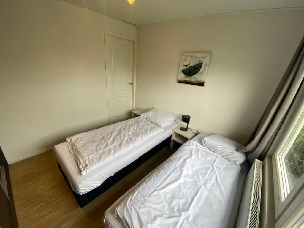 Slaapkamer met twee eenpersoonsbedden, een nachtkastje en een raam met uitzicht naar buiten.