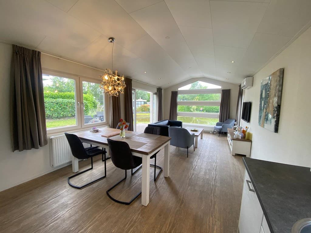 Ruime woonkamer met eettafel, bankstellen, grote ramen en moderne verlichting in EuroParcs Spaarnwoude