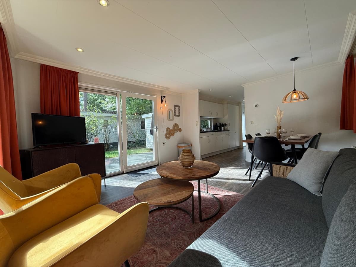 Woonkamer met kasten, een tv, een eettafel en uitzicht op de tuin door de glazen deuren.