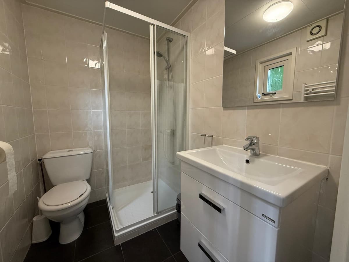 Moderne badkamer met douchecabine, wastafel en toilet, betegelde muren en donkere vloer.