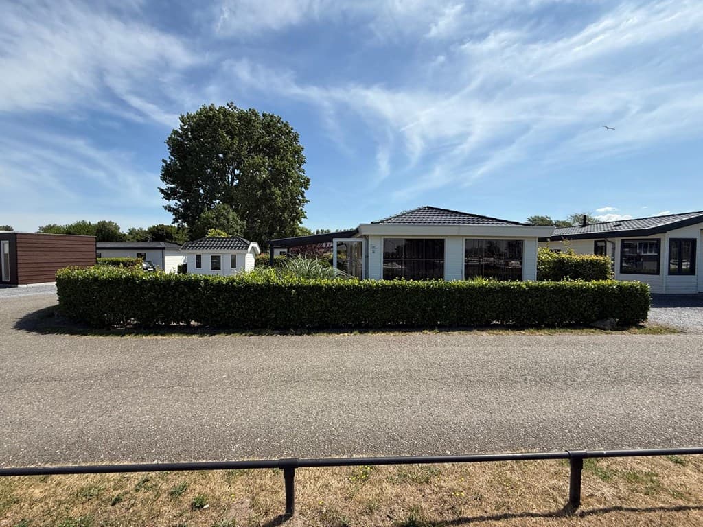 Buitenzicht op een vakantiewoning met tuin en bomen op EuroParcs De Biesbosch in Dordrecht onder een blauwe lucht