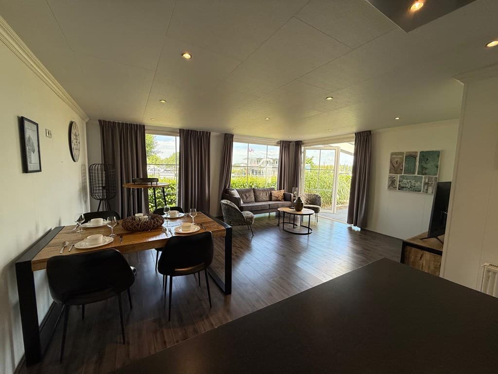 Licht en ruim interieur met een zithoek, eettafel en grote ramen met uitzicht op de natuur.