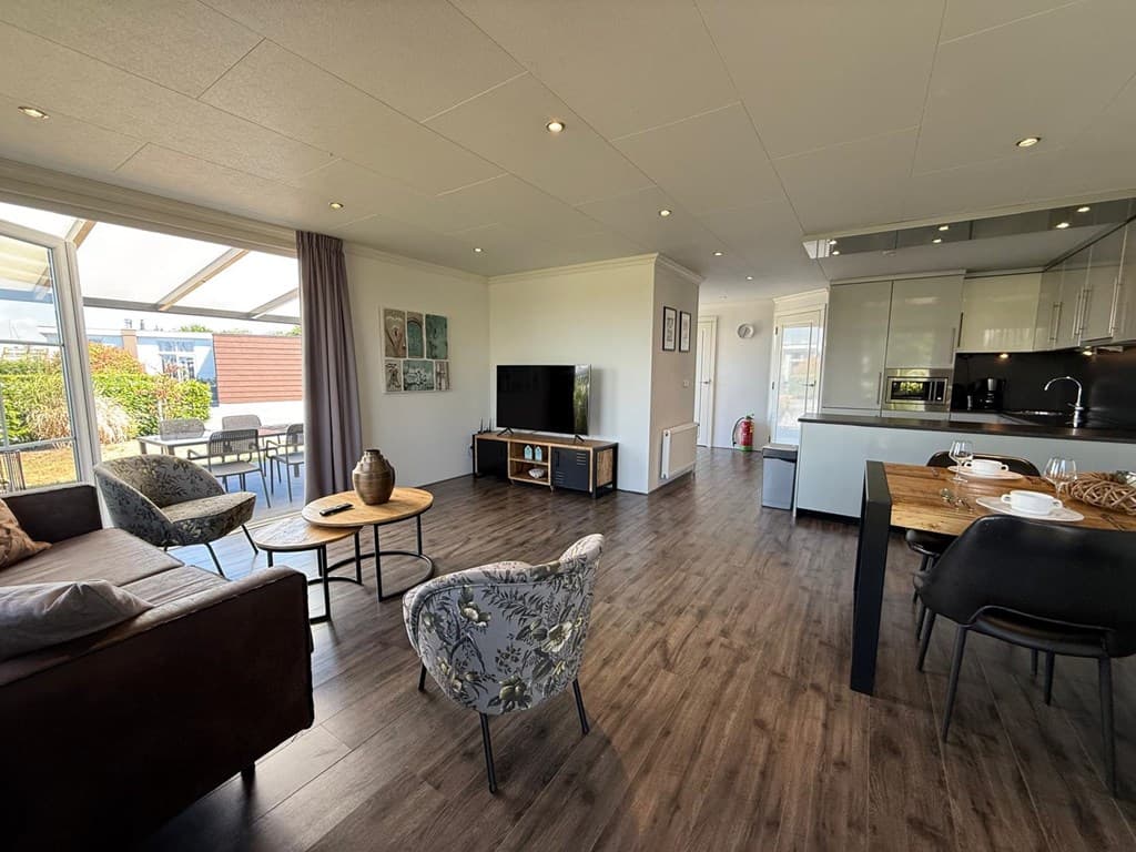 Moderne woonkamer met zithoek, eethoek en open keuken, deuren naar een terras met tuinmeubilair.