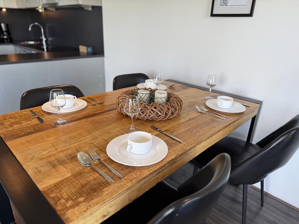 Eettafel met vier borden en glazen, omringd door zwarte stoelen in modern interieur.