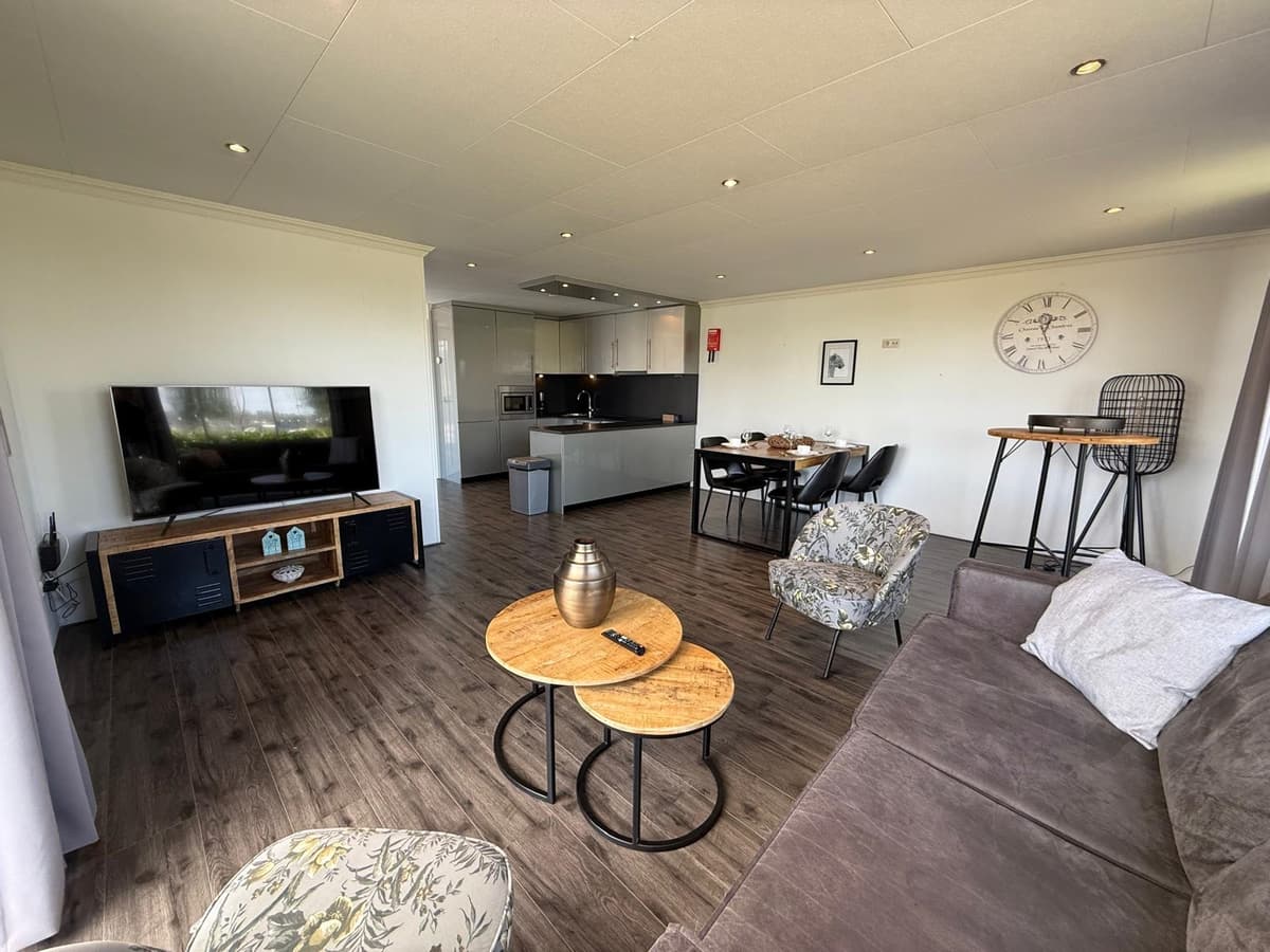 Moderne woonkamer met zithoek, eettafel en open keuken, grote ramen met uitzicht op de omgeving.