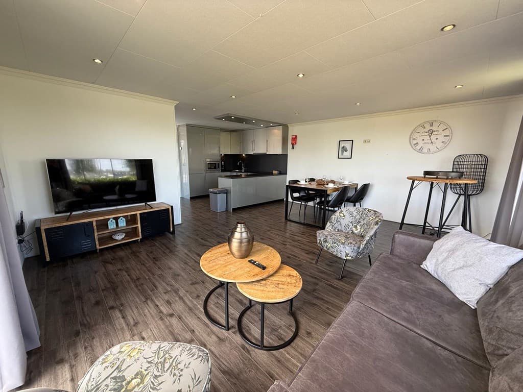 Moderne woonkamer met zithoek, eettafel en open keuken, grote ramen met uitzicht op de omgeving.