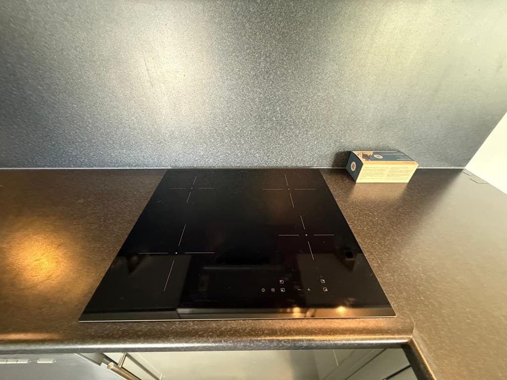 Inductiekookplaat in een moderne keuken met een zwarte werkblad en een doos in de hoek