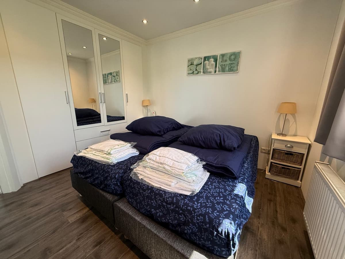 Slaapkamer met twee aparte bedden, een kledingkast met spiegel en een nachtlampje naast het raam.