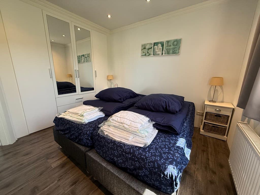 Slaapkamer met twee aparte bedden, een kledingkast met spiegel en een nachtlampje naast het raam.