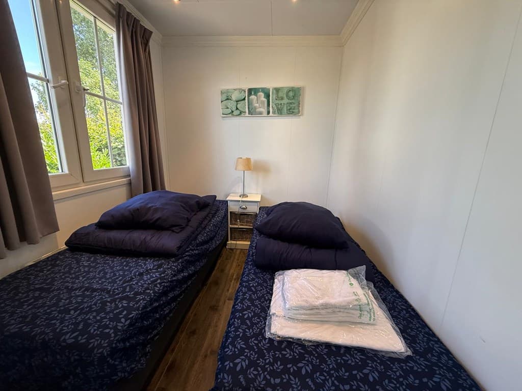 Slaapkamer met twee eenpersoonsbedden, een nachtkastje en een raam met uitzicht op de tuin.