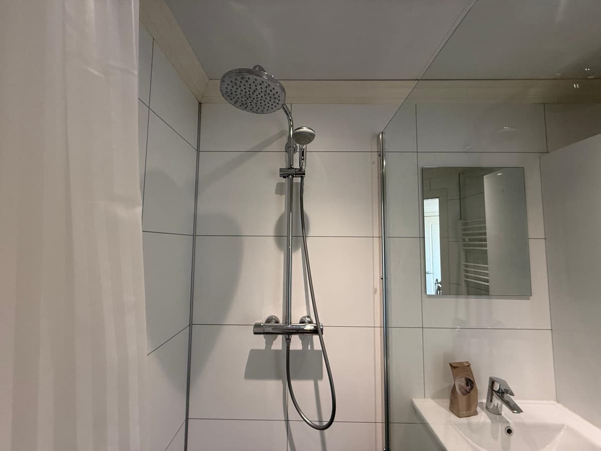 Inrichtingen van een moderne badkamer met douchekop, spiegel en wastafel in lichte tegels.