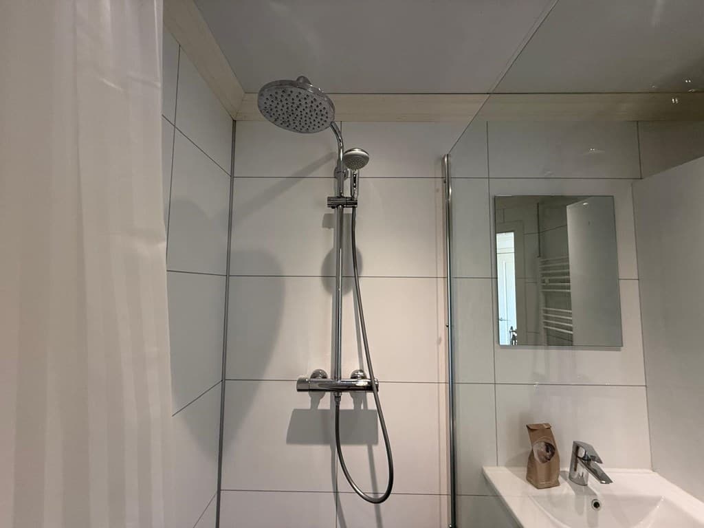 Inrichtingen van een moderne badkamer met douchekop, spiegel en wastafel in lichte tegels.