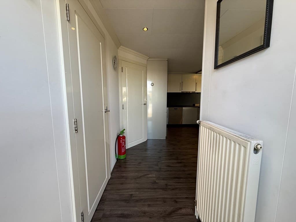 Overzicht van de hal in de woning met deuren naar andere ruimtes en een radiator aan de muur.