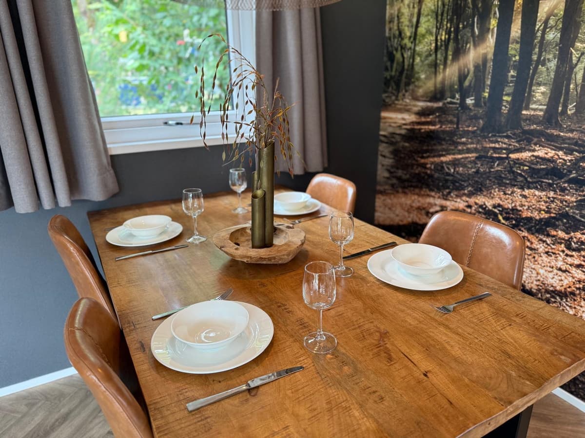 Eettafel met vier gedekte plaatsen en een decoratief stuk in een ruimte met natuurthema en ramen met uitzicht op buiten.