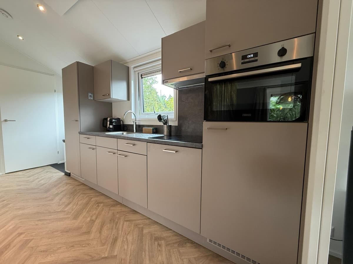 Moderne keuken met aanrecht, kastjes, oven, magnetron en uitzicht op een raam met groen buiten.