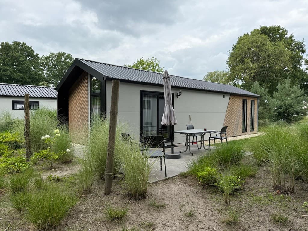 Moderne vakantiewoning met een terras en tuin, omgeven door gras en bomen, gelegen in een rustige omgeving.