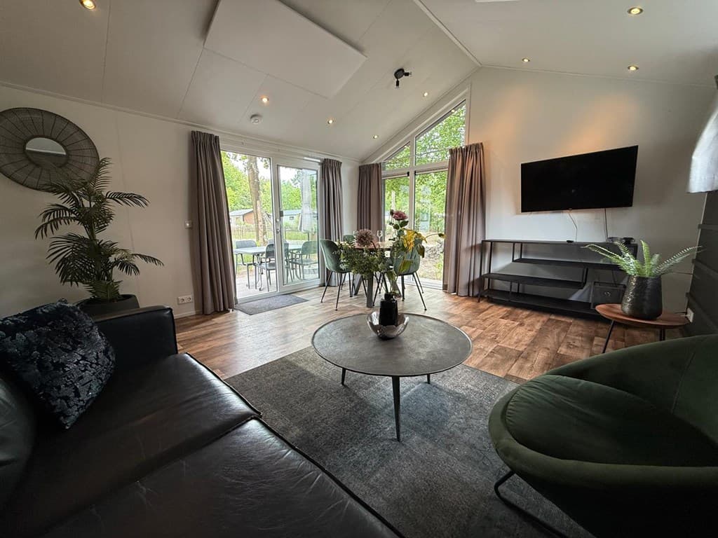Zitkamer met een moderne inrichting, banken, een ronde tafel en grote ramen die toegang geven tot de buitenruimte