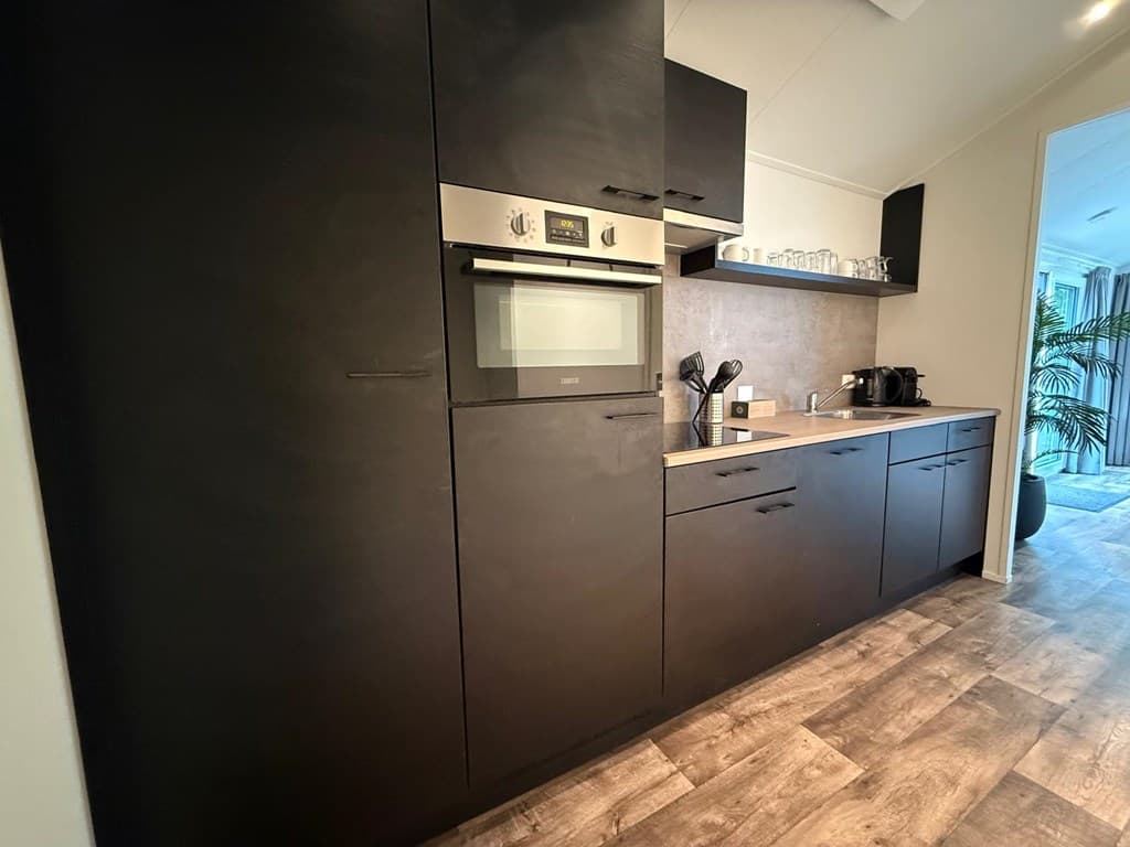 Moderne keuken met zwarte kasten, bovenkastjes en inbouwapparatuur, inclusief een oven en een koffiezetapparaat.