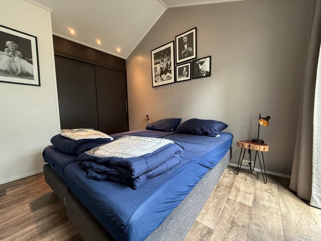 Sfeervolle slaapkamer met een groot bed, nachtkastje en foto's aan de muur.