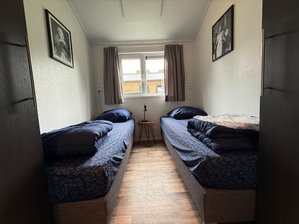 Slaapkamer met twee eenpersoonsbedden, een raam met gordijnen en een nachttafeltje in het midden.