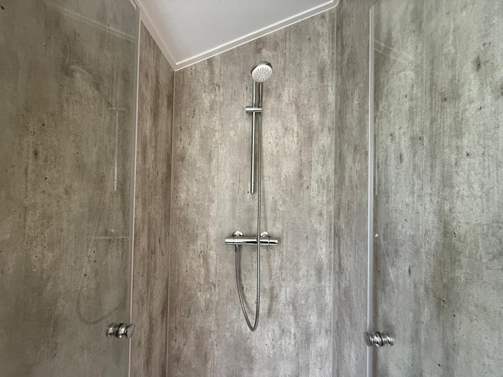 Douche met moderne wandafwerking en een handdouche in een lichte, neutrale kleurstelling.