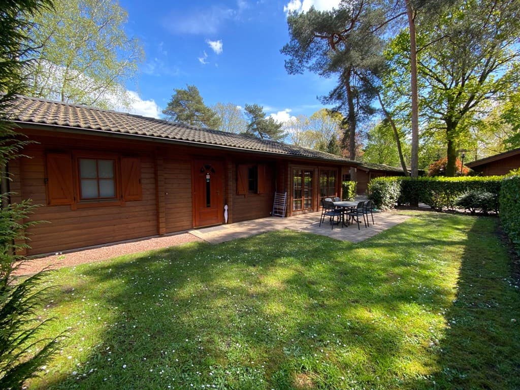Buitenzijde van een houten vakantiehuis met terras en tuinmeubilair, omringd door groen op EuroParcs De Achterhoek