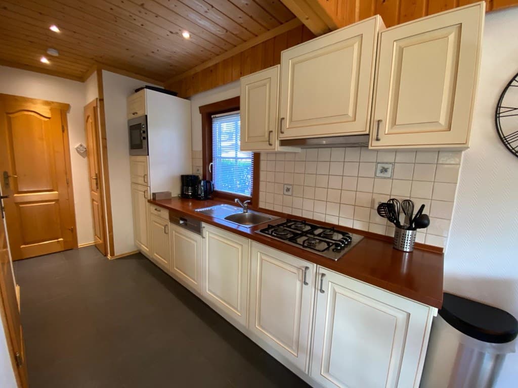 Keuken met beige kasten, gasfornuis, spoelbak en houten plafond in EuroParcs De Achterhoek, Lochem.