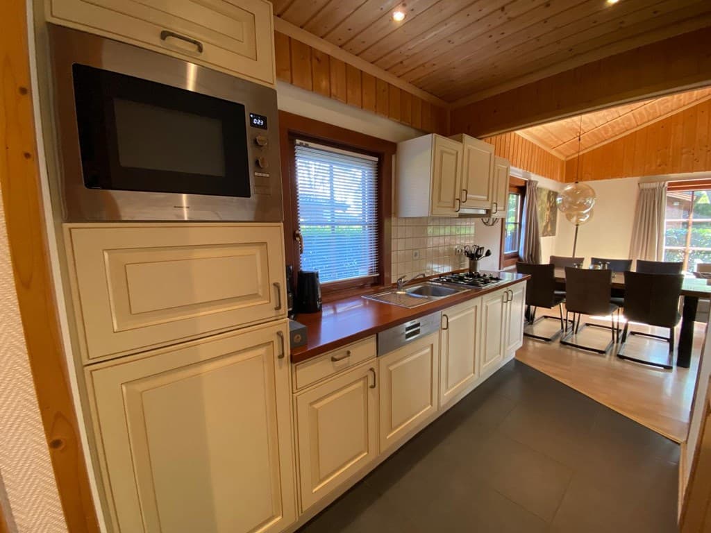 Ruime keuken met lichte kasten, gasfornuis, magnetron en uitzicht op de eetruimte met houten tafel en stoelen.