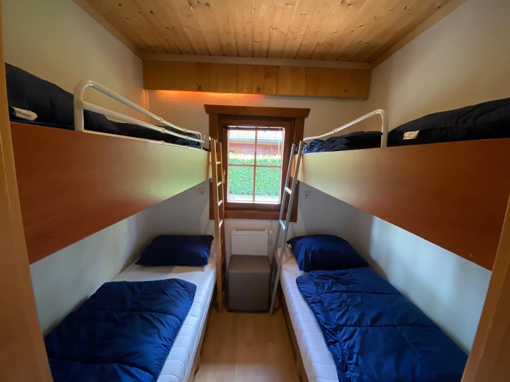 Slaapkamer met stapelbedden, twee bedden aan weerszijden en een raam met uitzicht op de buitenruimte.