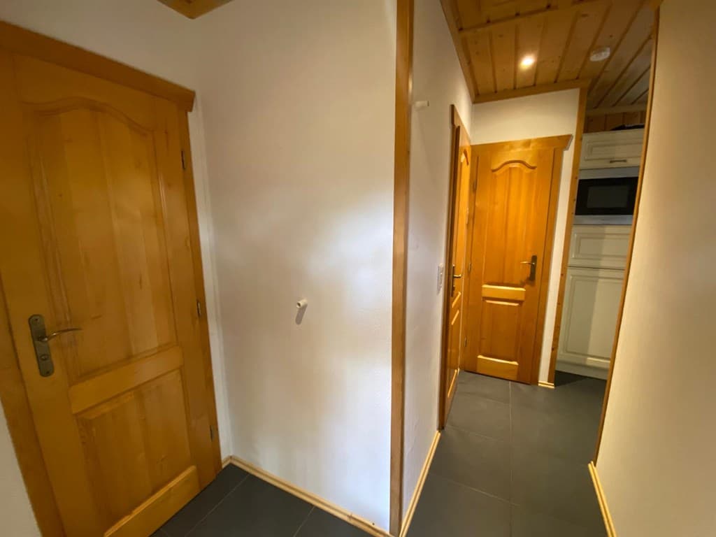 Ingang van een woning met houten deuren en zwart tegels op de vloer in een lichte gang.