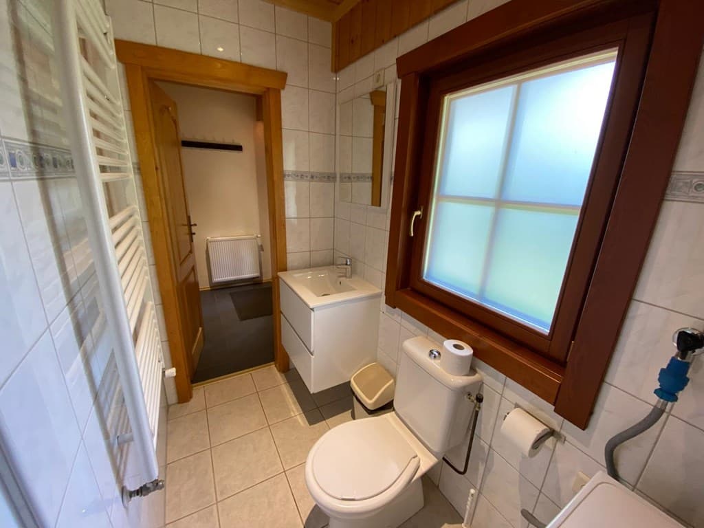 Badkamer met wastafelmeubel, toilet en tegelvloer, voorzien van een raam met houten omranding