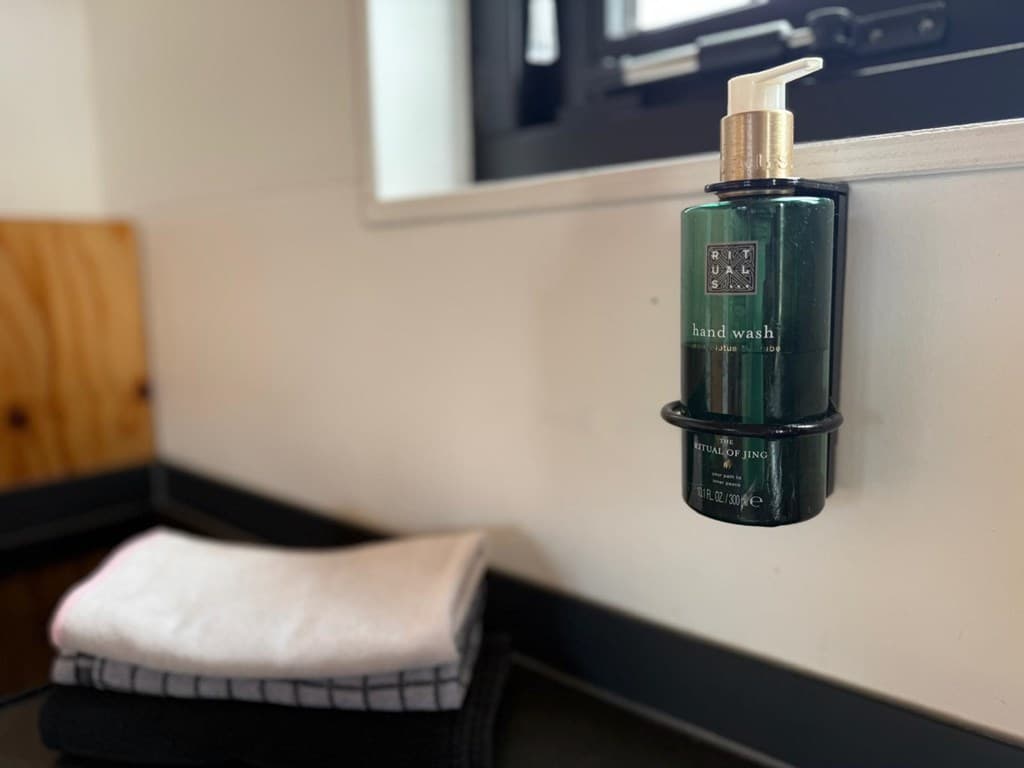 Fles handzeep in een dispenser naast een stapel handdoeken op een aanrecht met een raam op de achtergrond