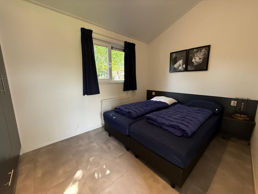 Slaapkamer met twee losse bedden, kastenwand, raam met gordijnen en twee zwart-wit fotos aan de muur