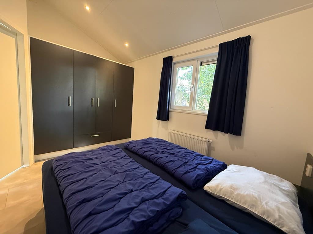 Slaapkamer met twee eenpersoonsbedden, kast met schuifdeuren en raam met uitzicht op buitenruimte