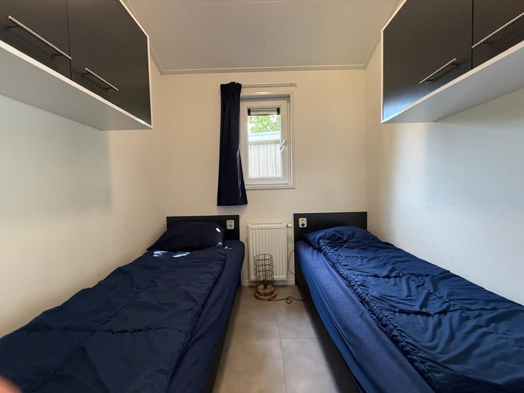 Slaapkamer met twee eenpersoonsbedden, wandplanken en een raam met gordijn