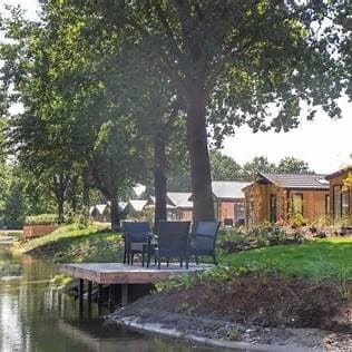 Uitzicht op een houten vlonder met stoelen aan het water, omringd door bomen en vakantiewoningen in de achtergrond.