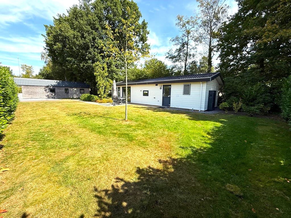 Tuin met een vrijstaande woning en een aanbouw, omgeven door bomen en grasvelden.