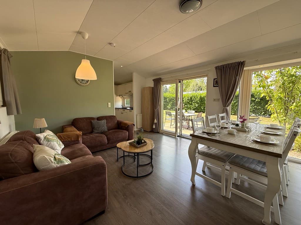 Gezellige woonkamer met bank, eettafel en toegang tot de tuin via dubbele deuren.
