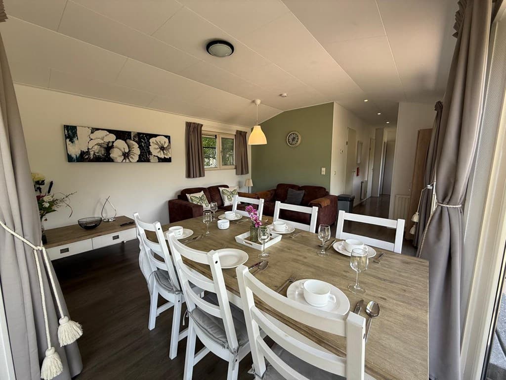 Eettafel met stoelen in lichte woonkamer met bank en lamp, raam met uitzicht op buitenruimte en moderne inrichting