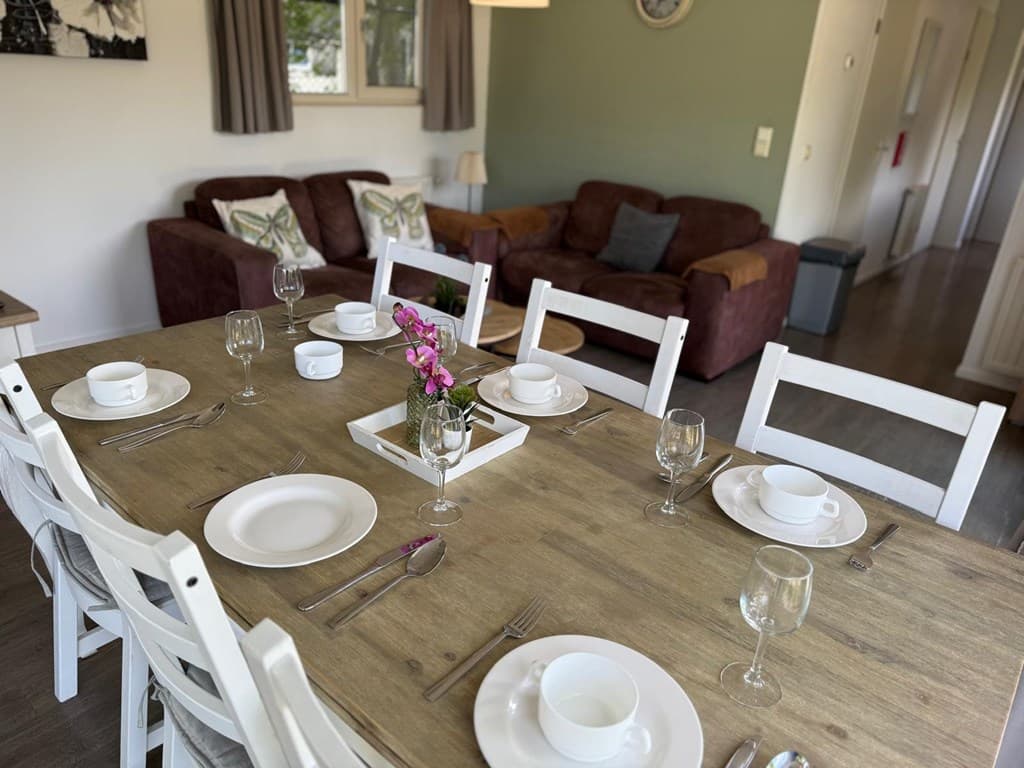 Eettafel met servies en glazen, zitbank in de achtergrond en een groene wand in de woonkamer.