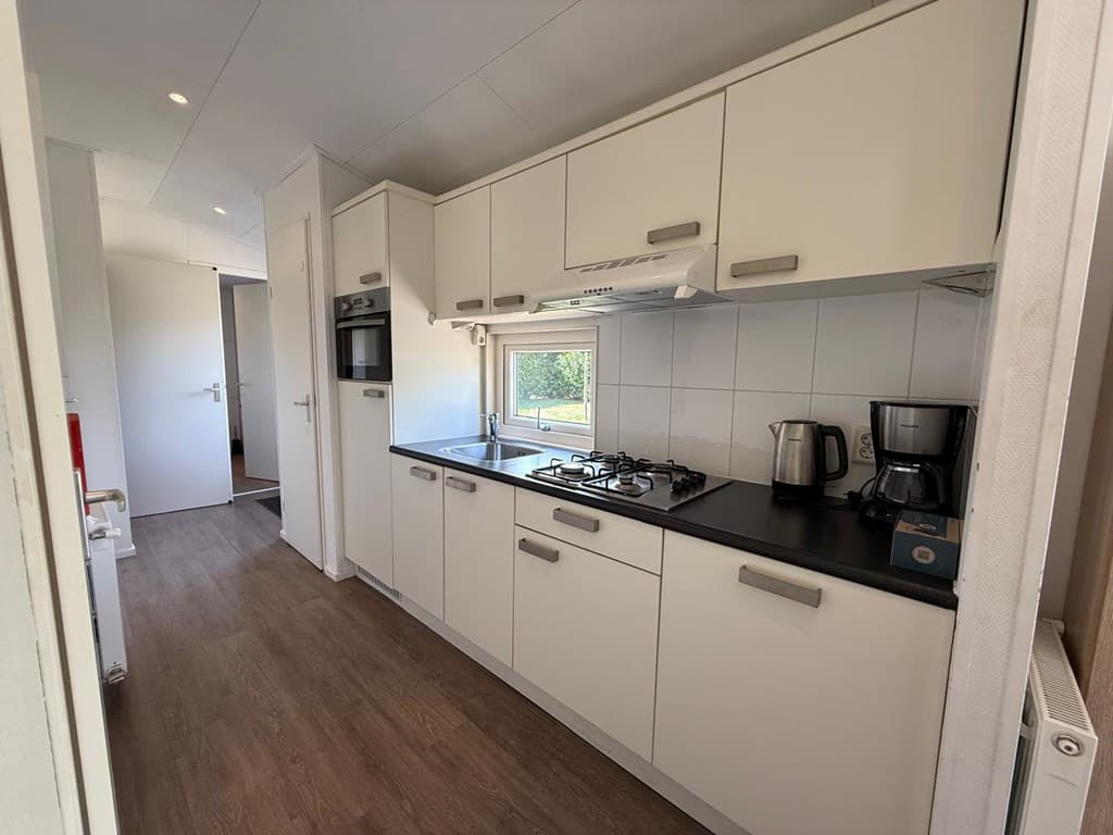 Moderne open keuken met witte kastjes, gasfornuis, inbouwoven en keukenapparatuur in EuroParcs Reestervallei.