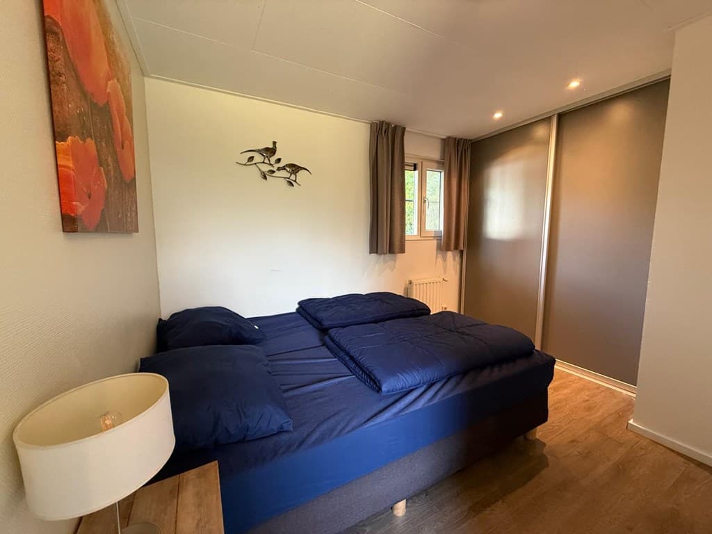 Slaapkamer met twee losse bedden, een nachtlampje en een kledingkast aan de muur met gordijnen bij het raam