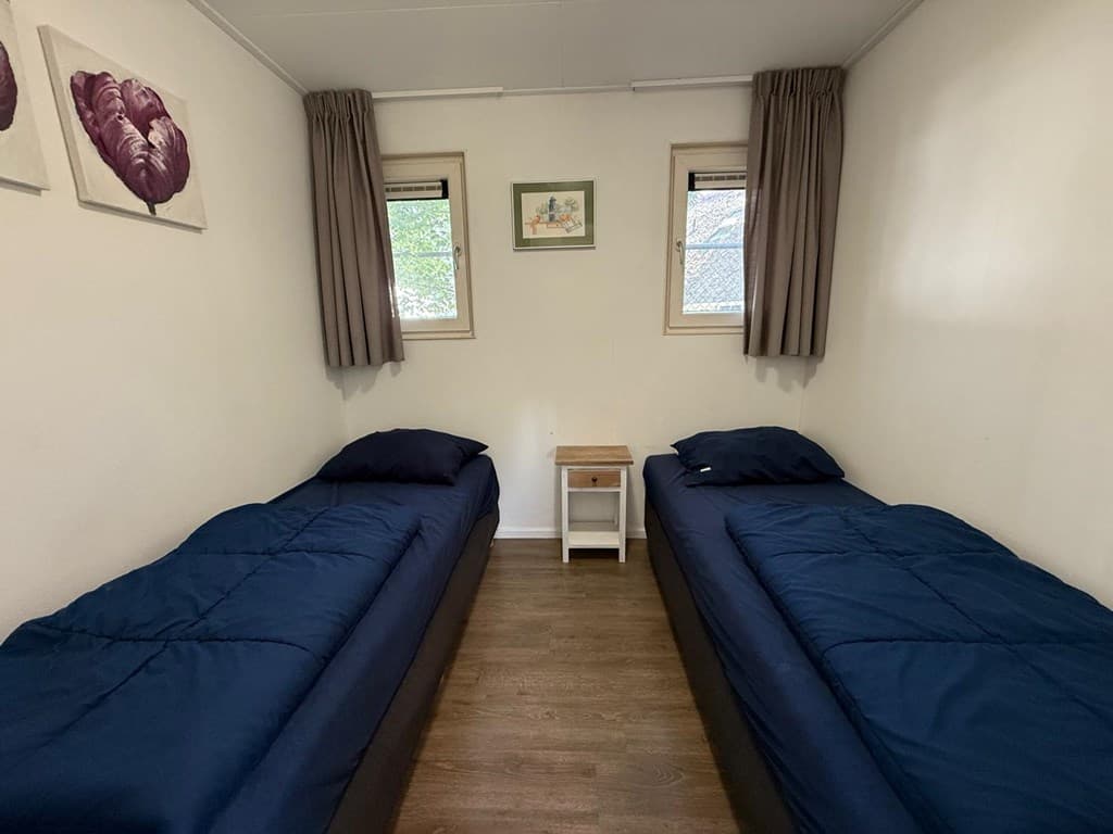 Slaapkamer met twee eenpersoonsbedden, houten vloer en twee raamdecoraties met gordijnen.